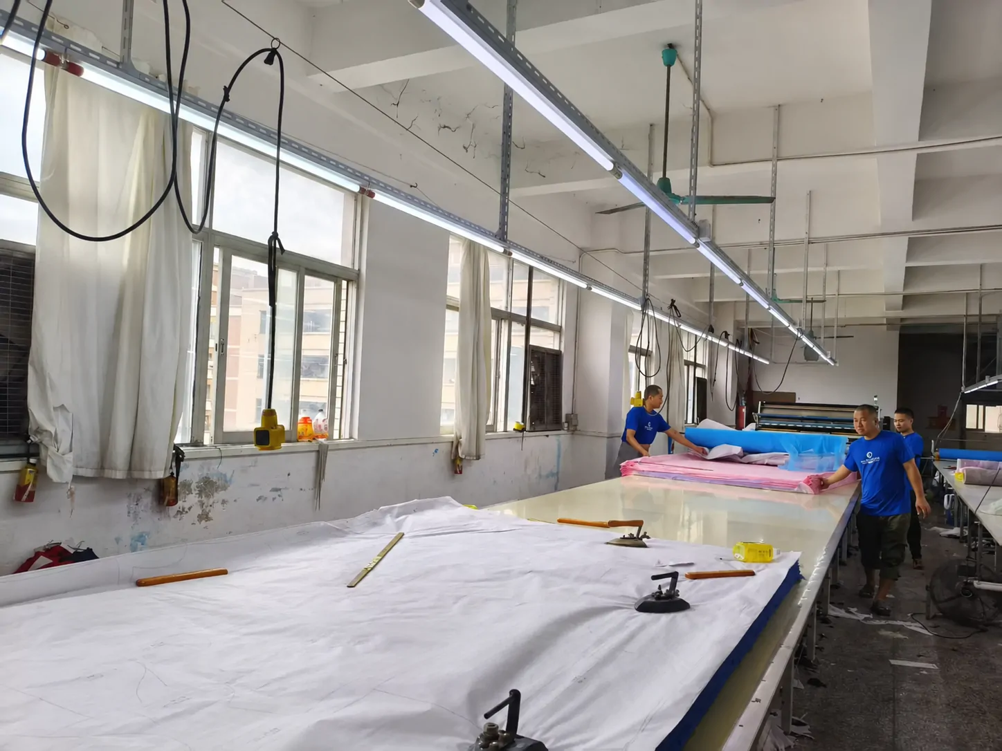 Workers spreading fabric across long preparation tables in our factory cutting room