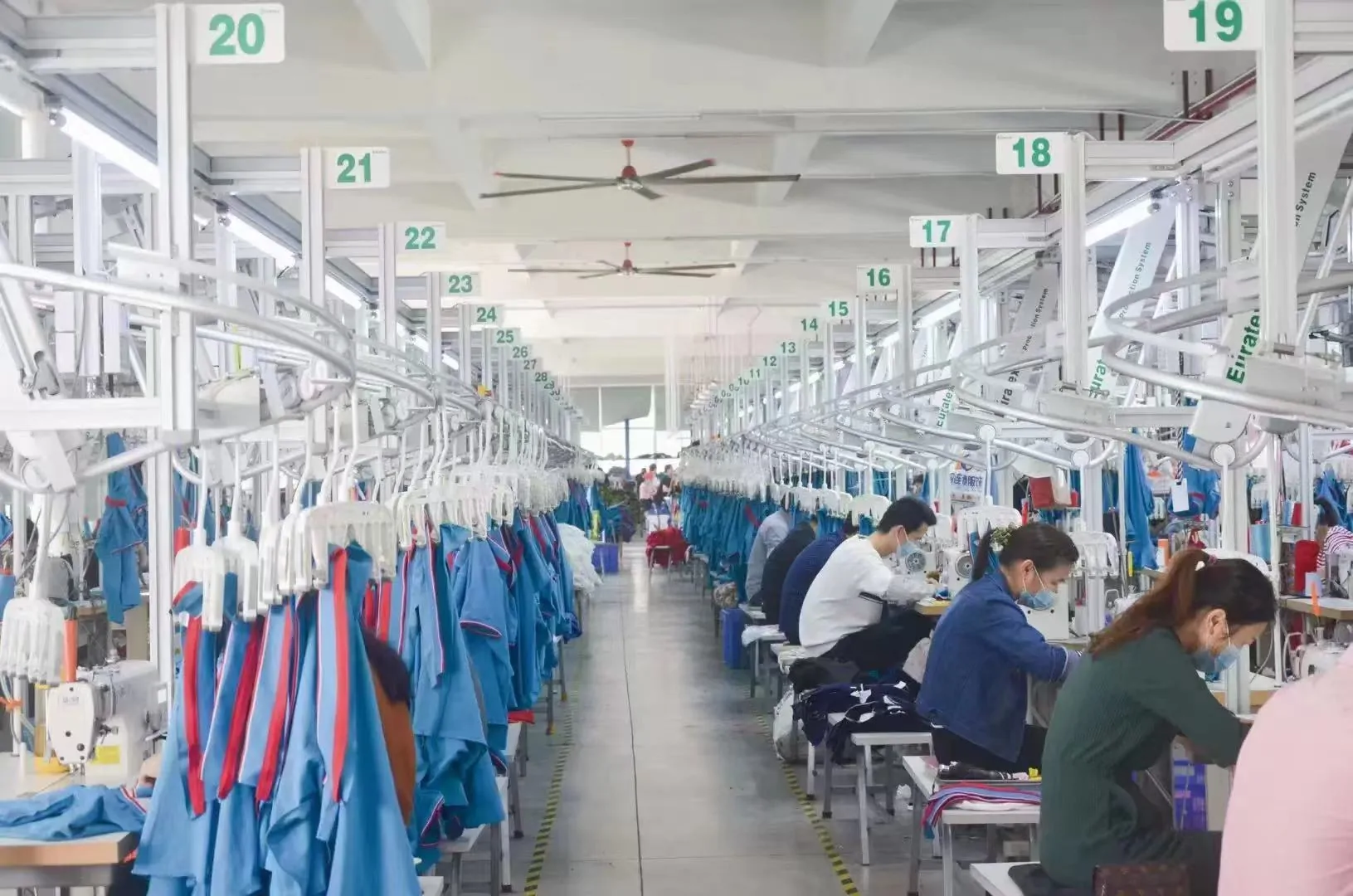 Numbered sewing stations in our factory with operators and blue garment panels in production