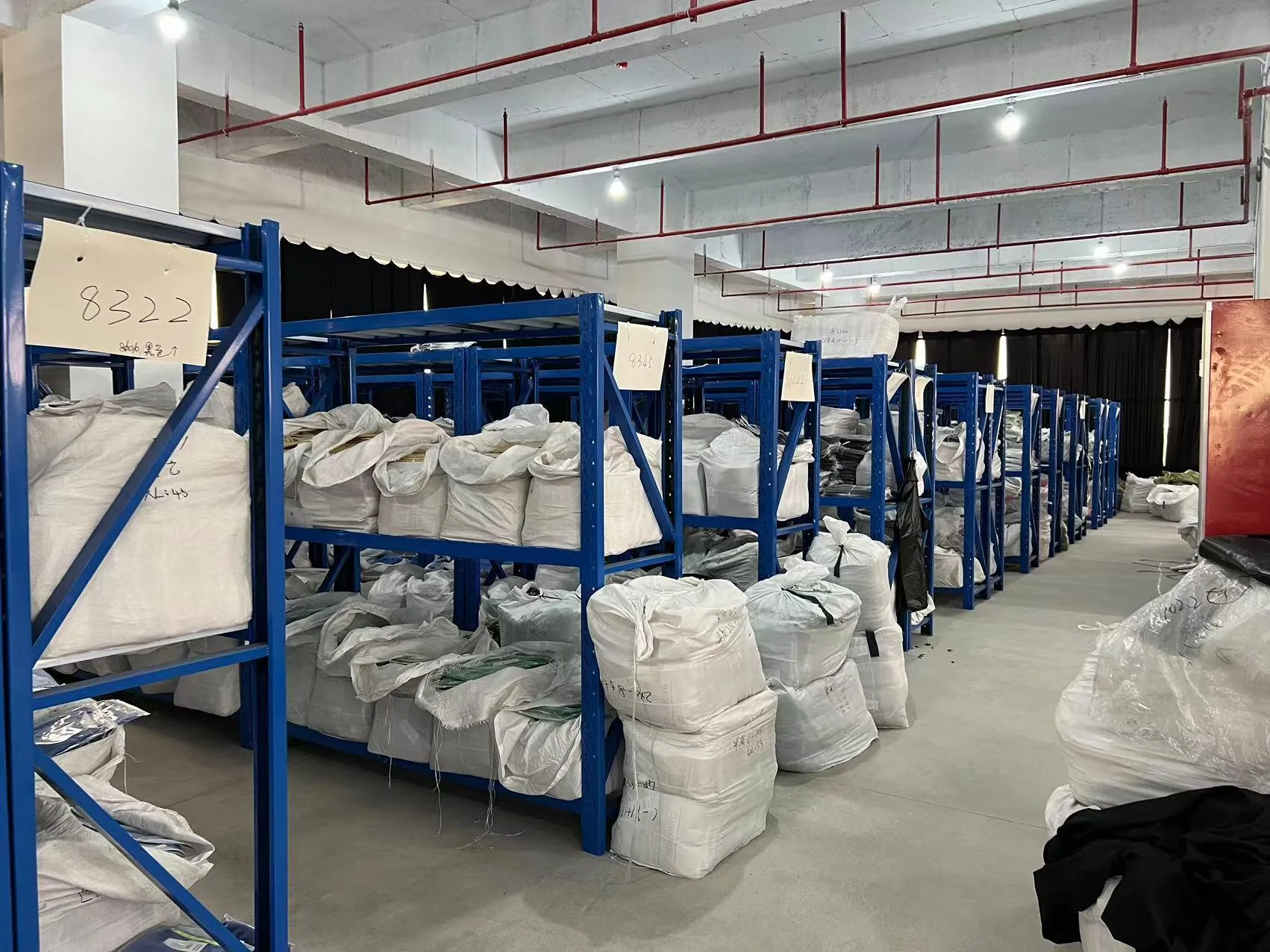 Blue storage racks in our factory holding bagged textile materials with handwritten identifiers