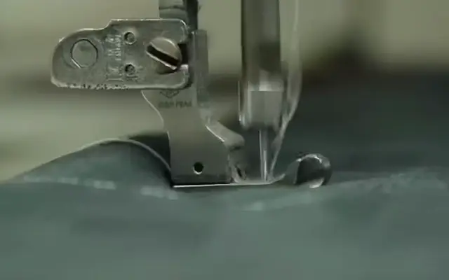 Presser foot and needle of a sewing machine stitching dark green knit fabric in SenLin’s workshop