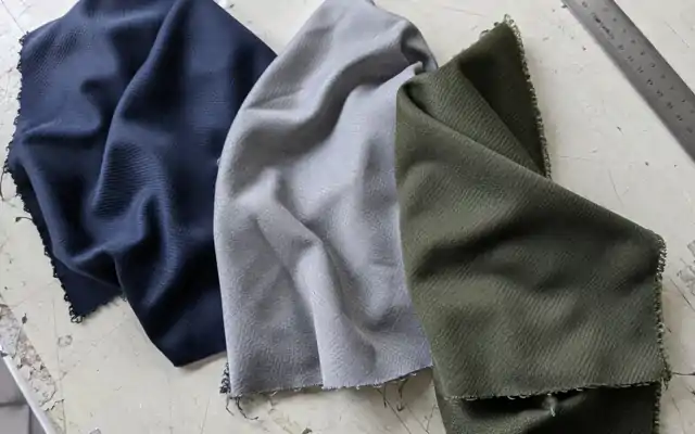 Raw-edged navy, grey and olive jersey swatches on a worn cutting table