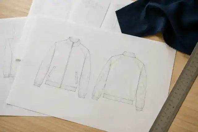 Garment flat drawings, pattern paper, ruler and fabric swatch on a desk