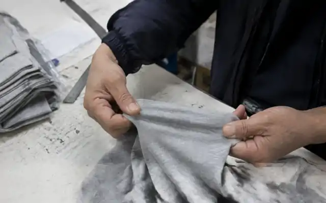 Hands gently stretching grey jersey fabric over a worktable