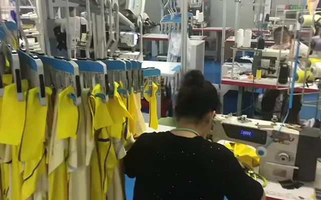 Garments hang on an overhead line beside a sewing operator at work on SenLin’s production floor