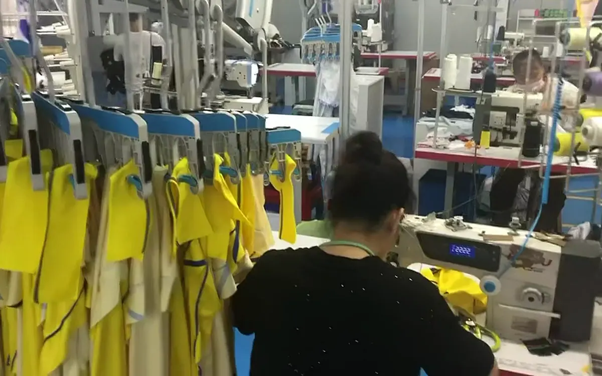 Garments hang on an overhead line beside a sewing operator at work on SenLin’s production floor